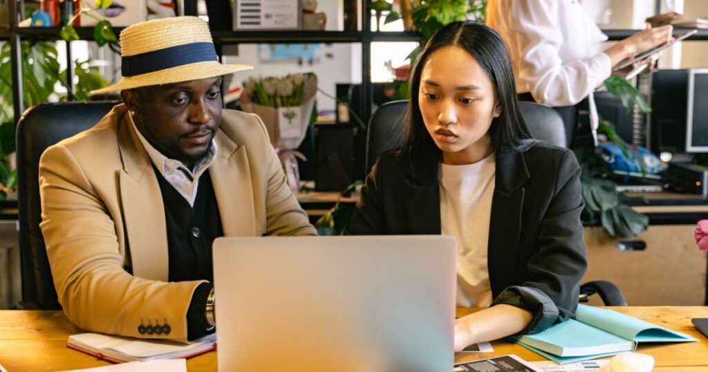 Two colleagues comparing Deel pricing on a laptop in a busy office
