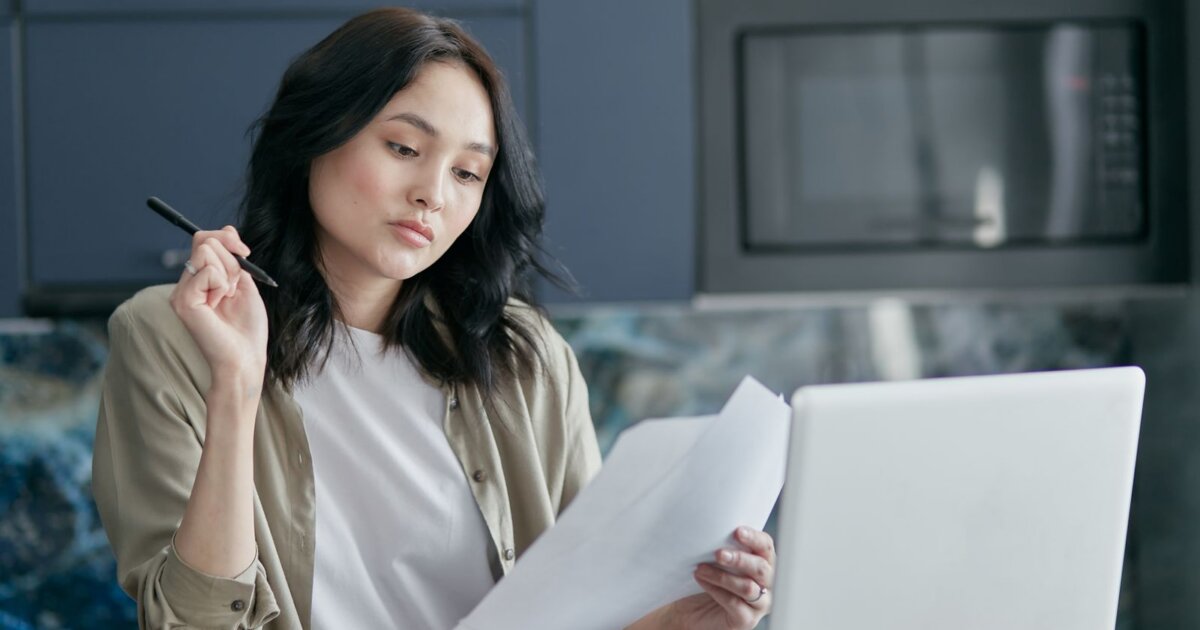 Woman reviewing paperwork beside a laptop while comparing Papaya Global alternatives